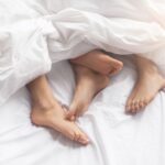 wit beddengoed waar twee paar voeten uitsteken die elkaar aanraken