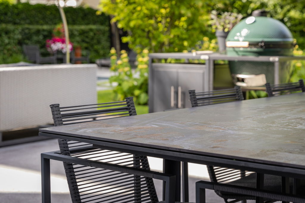 Een tafel met stoelen en een barbecue op de achtergrond.