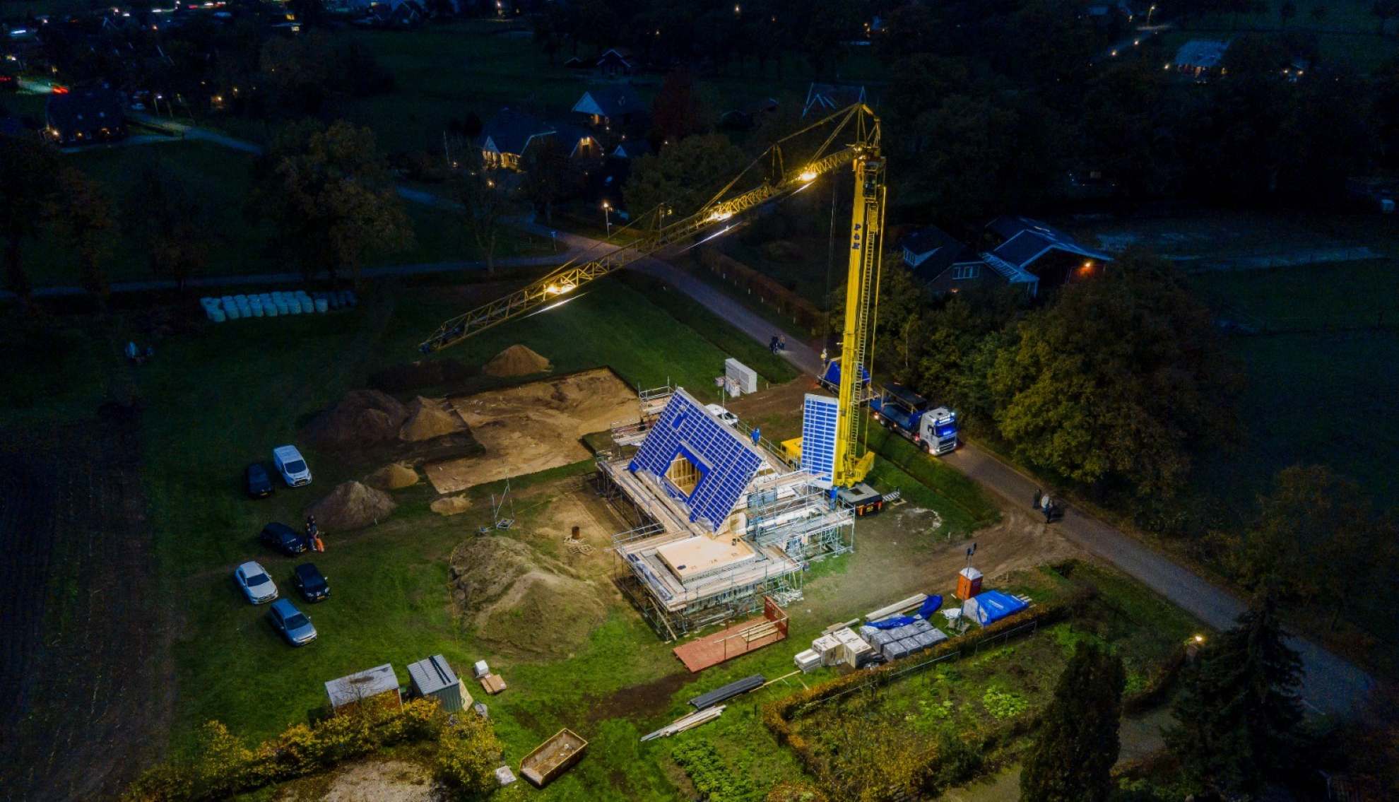 Snel prefab schuurwoning bouwen – nachtelijke montage op de bouwplaats met kraan en verlichte woning in aanbouw