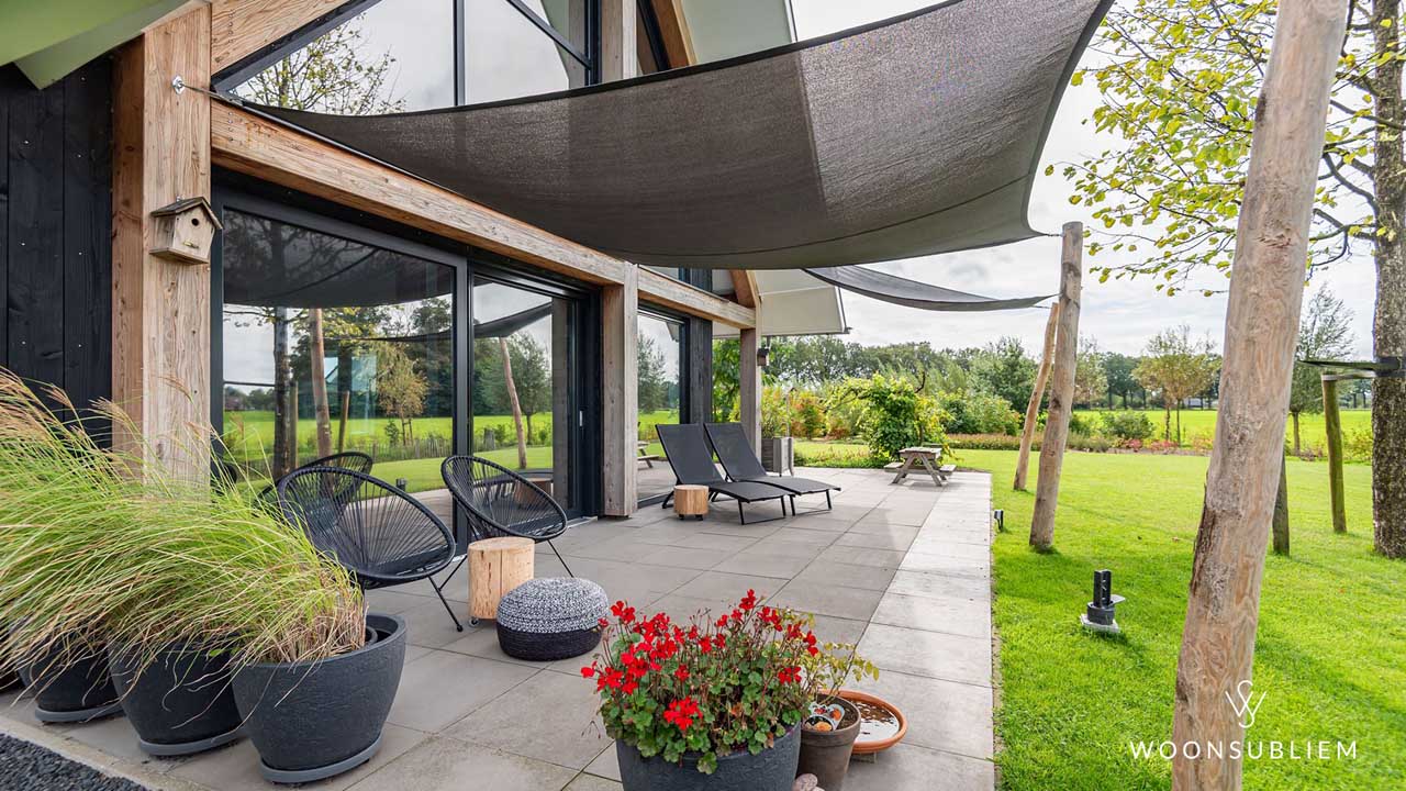Terras van schuurwoning met eiken spanten en schaduwdoeken – uitzicht op ruime, groene tuin.