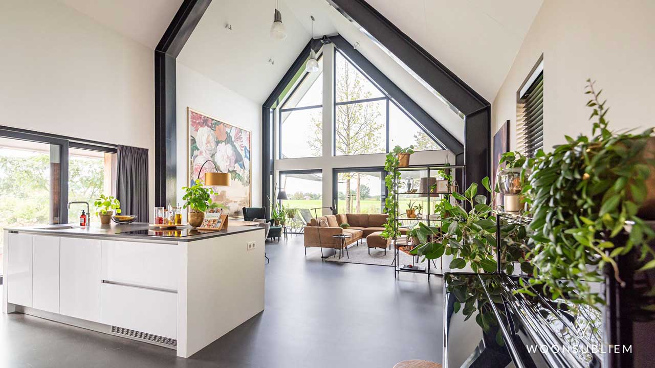 Lichte en ruime woonkamer van schuurwoning met hoge nok en eiken spanten – moderne inrichting met uitzicht op tuin.
